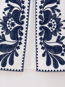 Detailed close-up of intricate navy blue paisley floral embroidery on a white vest