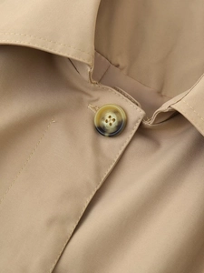 Detail shot of khaki trench coat showing the classic lapel and tortoiseshell resin button