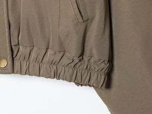 Détail de l'ourlet élastique et du bouton-pression en métal doré sur la veste