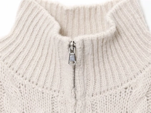 Detail view of cream knit sweater showing silver half-zipper and chunky cable knit texture