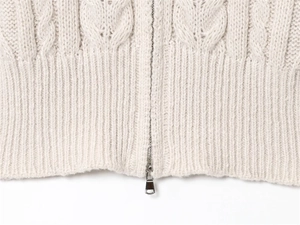 Close-up of cable knit sweater detail showing rib hem and silver metal zipper