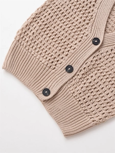 Détail du gilet beige tricoté montrant la texture crochetée et trois boutons noirs