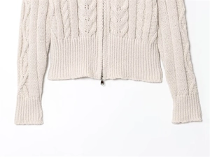 Detail of cable-knit texture and silver metal zipper on cream knit cardigan