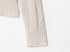 Detailed close-up of cable knit texture and ribbed cuffs on a beige knitted sweater