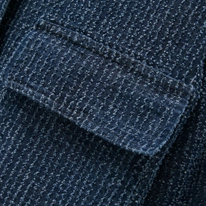 Close-up of deep blue textured denim jacket featuring lapel collar and flap pocket details