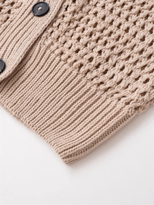 Détail macro du gilet en maille beige ajourée avec bords côtelés et boutons foncés