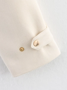 Détail du poignet de veste crème avec tissu texturé et bouton en métal doré chic