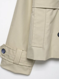 Detail view of khaki trench coat showing twill texture, cuff straps, and marbled buttons