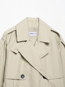 Detail of beige double-breasted trench coat showing lapel, shoulder tabs and fabric texture