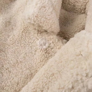 Detailed close-up of cream faux shearling coat texture with a clear resin button