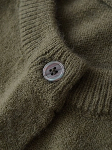 Close-up of olive green knit cardigan with plush texture and marble pattern button