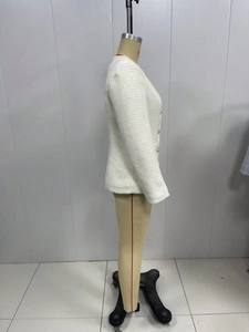 Detail of cream bouclé jacket fabric with weave texture and decorative metal buttons