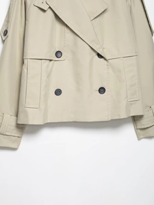 Detailed macro view of beige cropped trench coat featuring classic double-breasted buttons