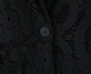 Close-up of black hollow lace blazer fabric with detailed floral texture and button