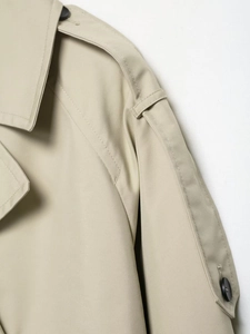 Detail view of khaki trench coat featuring shoulder epaulettes and classic lapel stitching