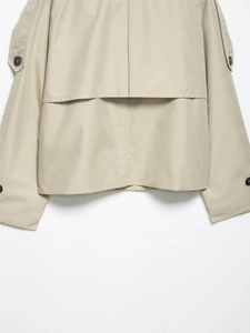 Detailed view of beige cropped trench coat featuring wind flaps and contrast buttons