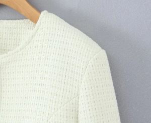 Close-up detail of cream tweed jacket woven texture and round neck stitching craftsmanship