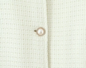 Close-up of white tweed texture and gold-rimmed pearl button on the jacket