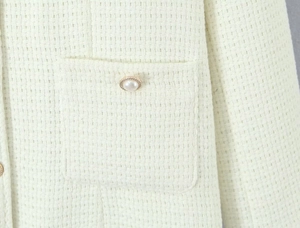 Close-up of cream tweed jacket texture with a pearl button on the front pocket