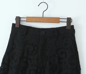 Detail of high-waist black lace trousers featuring intricate floral embroidery and button closure