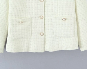 Detail of light green tweed jacket featuring pearl buttons with gold rims and woven texture