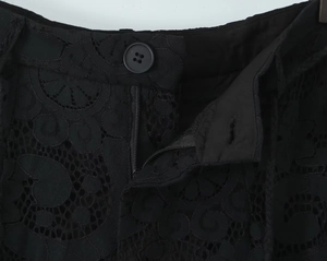 Close-up of black floral lace trousers featuring a round button and metal zipper detail