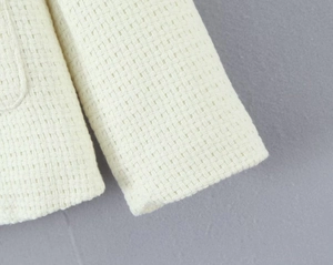 Close-up of off-white tweed jacket fabric showing intricate woven texture and sleeve detail