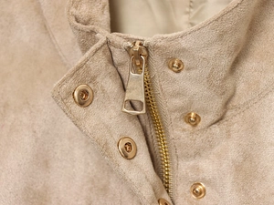 Détail d'une veste en daim beige avec fermeture éclair dorée et boutons-pression chic