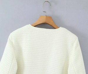 Detail view of cream tweed jacket shoulder and collar on a wooden hanger with rich texture