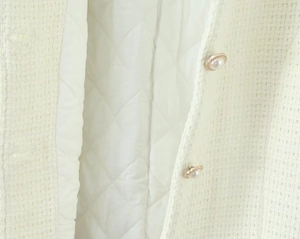 Detail of cream tweed jacket with gold-trimmed pearl buttons and diamond quilted lining
