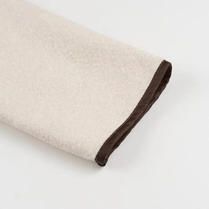 Close-up of fluffy beige faux shearling fabric with premium brown piped cuff stitching