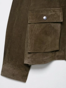 Detail of suede texture on dark olive jacket with metal button and pocket stitching