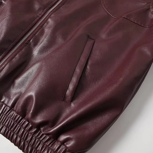 Macro detail of wine red PU leather jacket featuring metal zipper and ribbed elastic hem