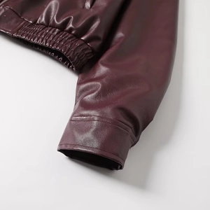 Detailed close-up of burgundy leather jacket featuring stitched elastic hem and premium texture