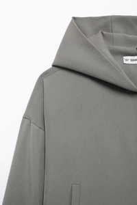 Détail de la veste à capuche grise montrant la texture du tissu et les coutures des épaules