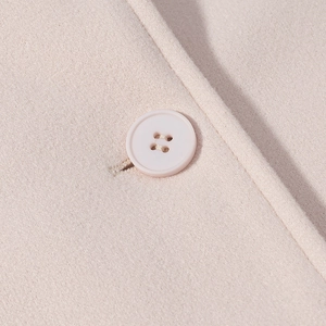 Detailed close-up of a resin button on light pink wool coat with neat stitching