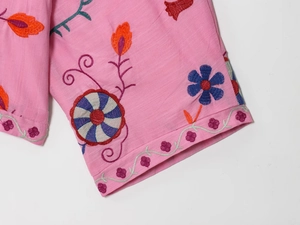 Detail of colorful floral embroidery and scalloped edges on a pink cotton shirt