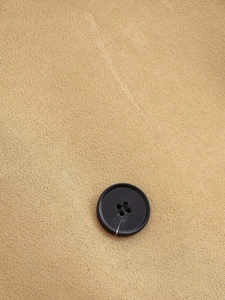 Detail of black four-hole button on khaki textured fabric of a short trench coat