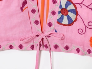 Detail of floral embroidery and bow tie closure on a pink cotton linen cardigan jacket