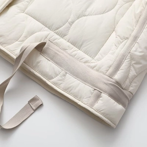 Detail of quilted hem on cream jacket featuring reinforced edges and woven belt