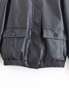Detail of black PU bomber jacket showing flap pockets, buttons and ribbed hemline