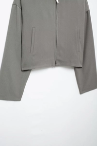 Détails d'une veste courte grise zippée montrant la texture du tissu et les poches