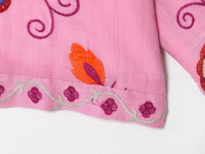 Detail of floral embroidery on pink cotton linen shirt sleeve with intricate needlework