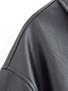 Close-up of double-stitched shoulder seams on a black PU leather jacket with fine texture
