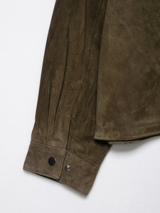Detailed close-up of olive suede jacket sleeve with black metal snap button and fine stitching