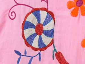 Detail of colorful floral embroidery and intricate patterns on pink cotton fabric