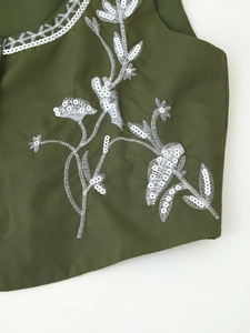 Detail of dark green vest with white floral embroidery and silver sequins on petals