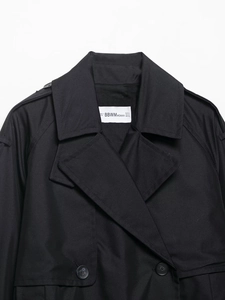 Gros plan du col d'un trench-coat noir avec épaulettes et étiquette de taille de marque
