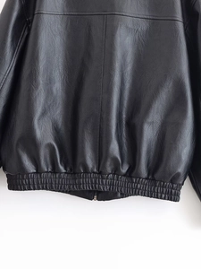 Detailed macro view of black PU leather jacket featuring elastic hem and metal zipper