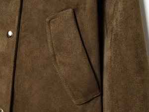 Detail of faux suede jacket showing pocket flap stitching and gold metal button hardware